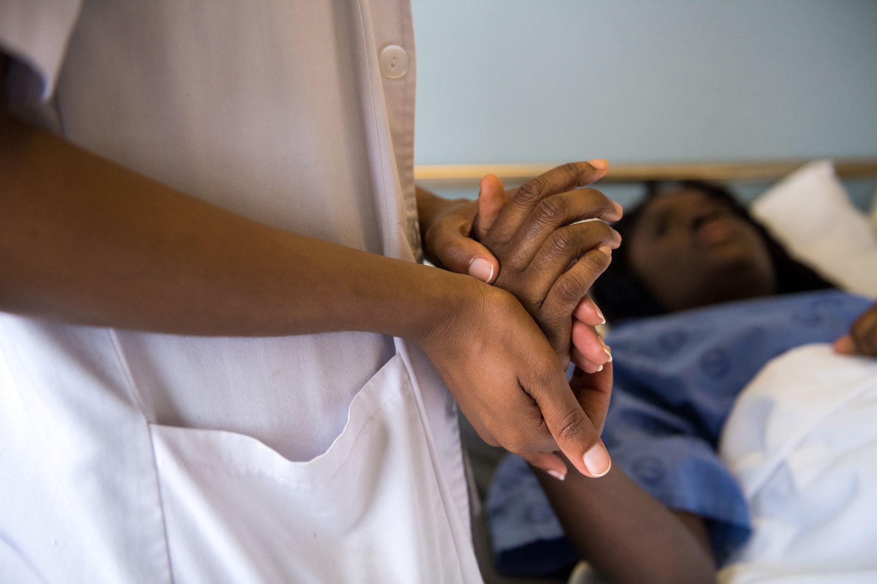 Clinician holds hand of woman lying in hospital bed