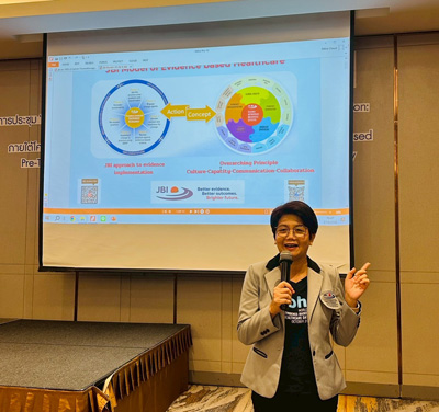 A/Professor Adchara Khammathit talks about JBI methodology at a workshop in front of a slide showing the JBI Model of Evidence-Based Healthcare 