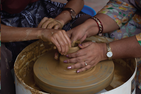 Close up of two sets of hands making a clay pot on a spinning wheel.