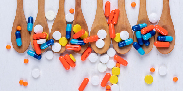 A collection of different pills spills over a row of wooden spoons representing the complexities of global medication safety