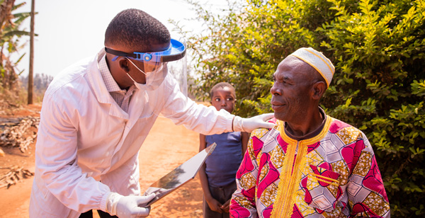 Clinician talks to a patient in an outdoor setting in Africa as part of the Global Evidence and Local Adaptation (GELA) Project
