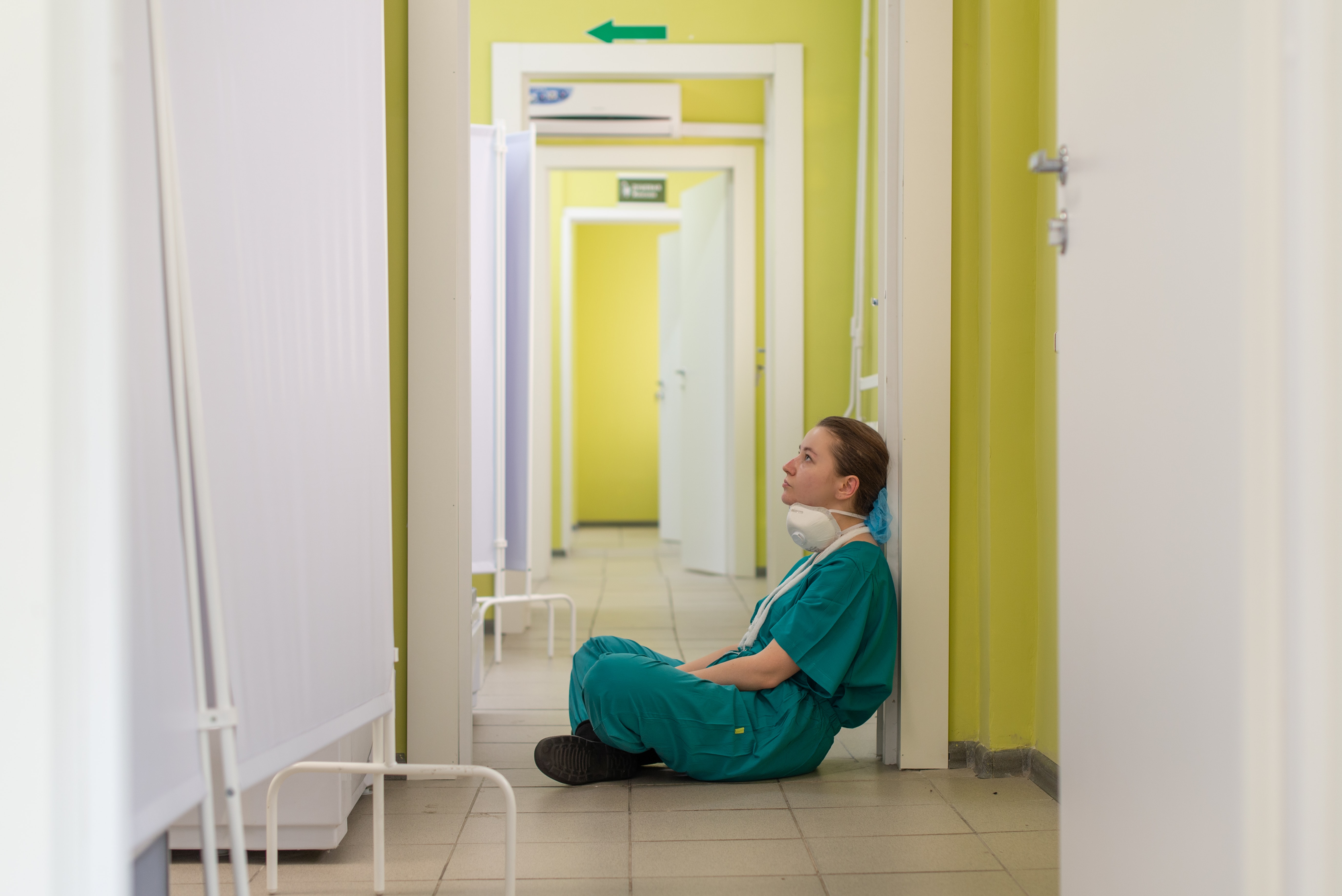 Clinician sitting on the floor in scrubs outside hospital room