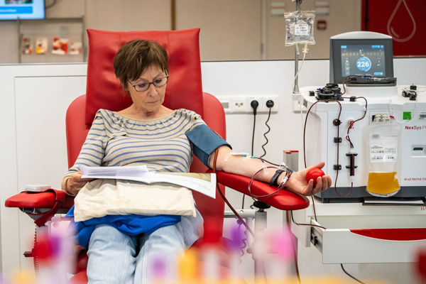 A female sits reading a magazine in red chair while donating plasma