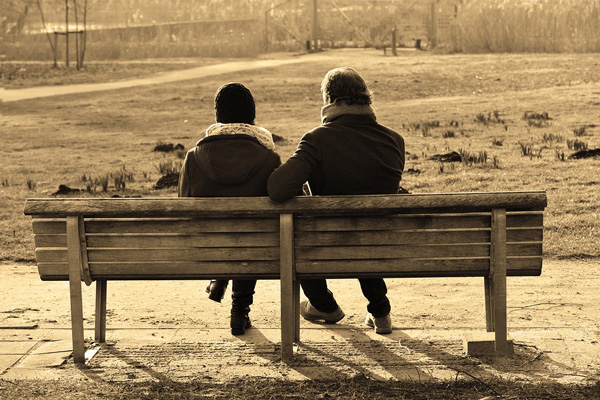 Two people sit close to each other on a park bench