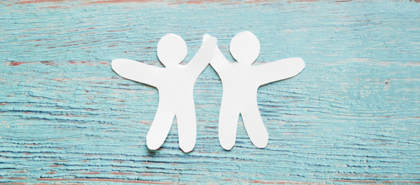 Two paper cut out people holding hands representing Survivor driven collaboration